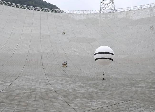 A karbantartót ballonhoz kötik, hogy így csökkentsék a súlyát, miközben a törékeny antennán dolgozik.