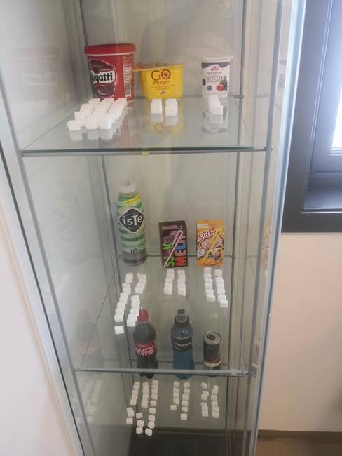 Egy fogorvosi rendelő vitrinje, mely mutatja, hogy mennyi cukor található a különféle termékekben.
