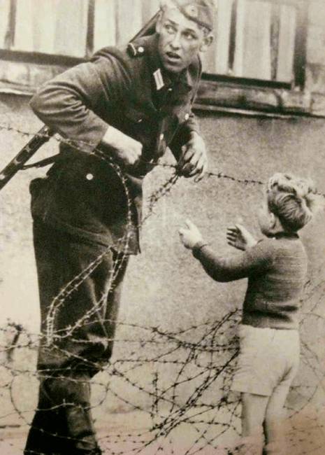 Egy katona segít átjutni egy fiúnak a berlini falon.