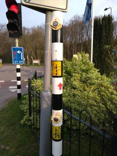 Ennél az úttestet keresztező bicikliútnál két különböző magasságban elhelyezett nyomógomb található a lámpán: az egyik a biciklisek, a másik a lovasok számára.